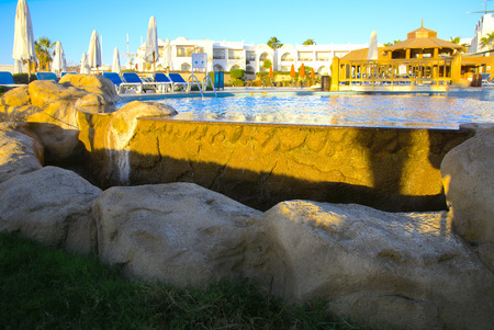 Sharm el-Sheikh, Egypt - March 14, 2018.  Beautiful pool in Cyrene Grand Hotel with clear blue water on the background of the sea, blue sky and green palm trees. Beach chaise longue.のeditorial素材