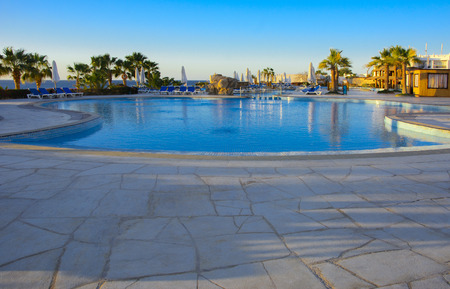 Sharm el-Sheikh, ?????? - 14 ????? 2018 ????. Beautiful pool in Cyrene Grand Hotel with clear blue water on the background of the sea, blue sky and green palm trees. Beach chaise longue.のeditorial素材
