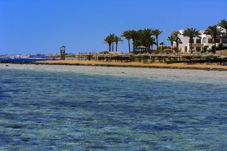 Sharm el-Sheikh, Egypt - March 14, 2018. A row of straw umbrellas to protect against overheating on a sandy beach against a blue sky and blue sea. The concept of summer holidays, tourism, travel.のeditorial素材