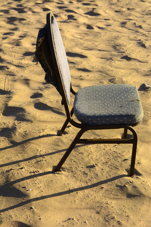 An old wicker chair from the vine is thrown out on an empty seashore against a background of yellow sand. Abandoned, unnecessary things. Vacation, tourism.の写真素材
