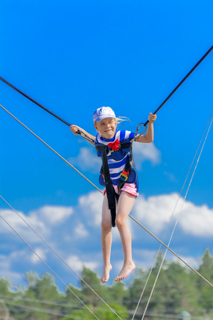 Zarechany, Ukraine - June 10, 2018. Children jumping on a trampoline with rubber ropes against the blue sky. Adventure and extreme sports. The concept of summer recreation, jumping.のeditorial素材