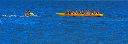 Odessa, Ukraine - August 8, 2018. Tourists having fun and enjoy riding a red and yellow inflatable banana, which transports the scooter by sea. The concept of summer holidays, vacation and travelのeditorial素材