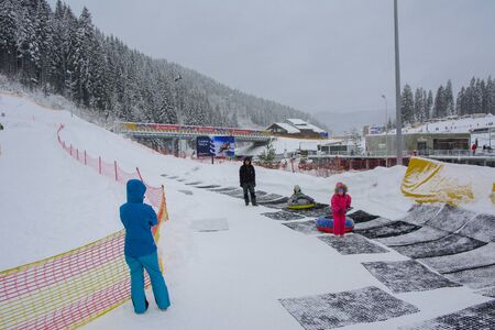 Bukovel, Ukraine - December 26, 2018. Little girls have fun on snow slides, ride inflatable chambers and enjoy the fresh snow on a beautiful winter day in the mountains. Winter holiday conceptのeditorial素材