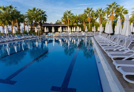 Alanya, Turkey - October 05, 2018. Beautiful pool in Kirman Sidera Luxury hotel with clear blue water on background of sea, blue sky and green palm trees. Beach chaise longue, summer vacation, tourismのeditorial素材