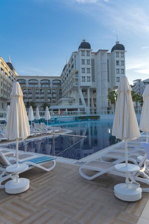 Alanya, Turkey - October 05, 2018. Beautiful pool in Kirman Sidera Luxury hotel with clear blue water on background of sea, blue sky and green palm trees. Beach chaise longue, summer vacation, tourismのeditorial素材