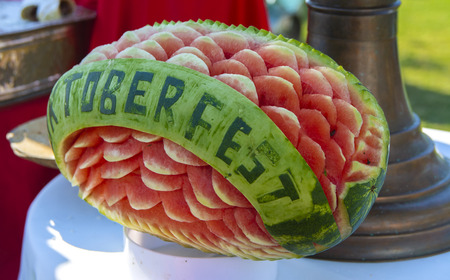 An originally carved large ripe watermelon in the shape of a flower on a white plate against the background of the table. The concept of delicious and healthy food.の写真素材