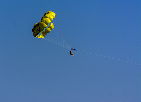 A skydiver flies with a colorful parachute tied to a speedboat on the sea against the backdrop of mountains with a blue sky. The concept of summer holidays, vacation, tourism.のeditorial素材