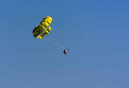 A skydiver flies with a colorful parachute tied to a speedboat on the sea against the backdrop of mountains with a blue sky. The concept of summer holidays, vacation, tourism.のeditorial素材