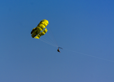 A skydiver flies with a colorful parachute tied to a speedboat on the sea against the backdrop of mountains with a blue sky. The concept of summer holidays, vacation, tourism.のeditorial素材
