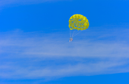 A skydiver flies with a colorful parachute tied to a speedboat on the sea against the backdrop of mountains with a blue sky. The concept of summer holidays, vacation, tourism.のeditorial素材