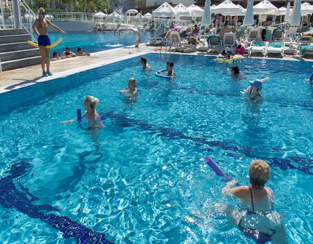 Alanya, Turkey - October 05, 2018. A group of people is engaged in aqua aerobics in the blue clear water of the pool at Kirman Sidera Luxury Spa. Fitness concept, summer vacation, sport, tourismのeditorial素材