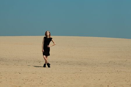 Fashion shot in the desert. A beautiful sexy girl in a black dress. The girl in the desert in fashionable clothes for advertising.の写真素材