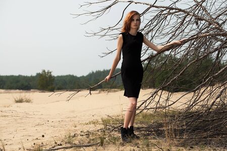 Fashion shot in the desert. A beautiful sexy girl in a black dress. The girl in the desert in fashionable clothes for advertising.の写真素材