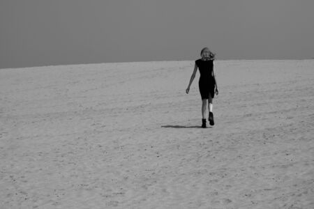 Fashion shot in the desert. A beautiful sexy girl in a black dress. The girl in the desert in fashionable clothes for advertising.の写真素材