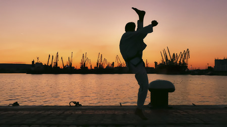 martial artist training alone on the sea pier, practicing his moves on sunset and port cranes background.の写真素材