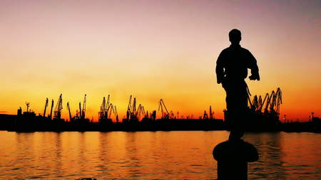 martial artist training alone on the sea pier, practicing his moves on sunset and port cranes...