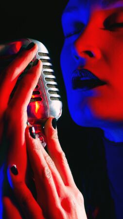 Close up of beautiful female woman singer mouth with red lips singing into a vintage microphone in a night clubの写真素材
