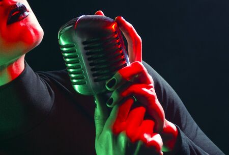 Close up of beautiful female woman singer mouth with red lips singing into a vintage microphone in a night clubの写真素材