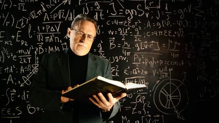 Medium shot of male university professor with book in hands. Math formulas on blackboard. Knowledge and On-line education concept.の写真素材