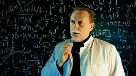 Medium shot of male university professor in white coat. Math formulas on blackboard. Knowledge and On-line education concept.の写真素材