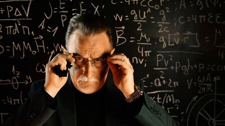 Medium shot of male university professor. Math formulas on blackboard. Knowledge and On-line education concept.の写真素材