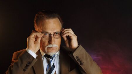 Mature gentleman on dark background. Medium shot portrait elderly elegant man. Handsome gray haired old businessman in glasses.の写真素材