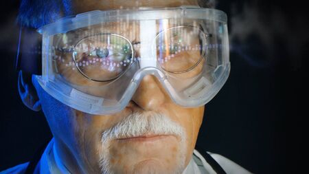 Mature doctor in augmented reality glasses on dark background. Close up portrait elderly scientist in high tech laboratory. Handsome gray haired doctor in augmented reality glasses looking at screen.の写真素材