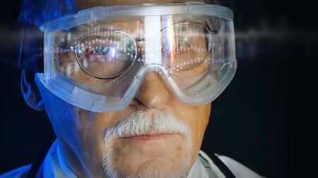 Mature doctor in augmented reality glasses on dark background. Close up portrait elderly scientist in high tech laboratory. Handsome gray haired doctor in augmented reality glasses looking at screen.の写真素材