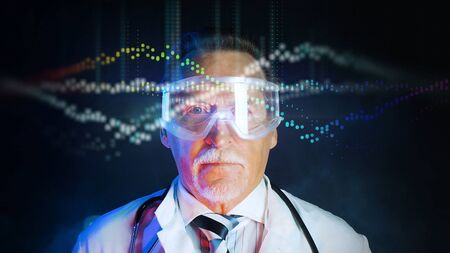 Mature doctor in white medical lab coat on dark background. Medium shot portrait elderly scientist in high tech laboratory. Handsome gray haired old doctor in mask looking at augmented reality screen.の写真素材