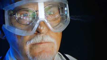 Mature doctor in augmented reality glasses on dark background. Close up portrait elderly scientist in high tech laboratory. Handsome gray haired doctor in augmented reality glasses looking at screen.の写真素材