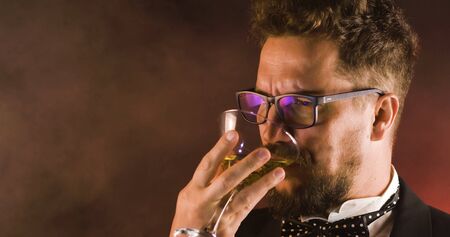 Handsome man in suit drinking champagne on black background. Portrait of elegance gentleman with glasses. Confident adult man in suit holding glass of champagne in studio. Luxury party.の写真素材