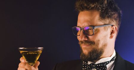Handsome man in suit drinking champagne on black background. Portrait of elegance gentleman with glasses. Confident adult man in suit holding glass of champagne in studio. Luxury party.の写真素材