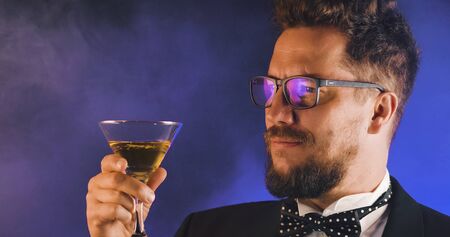 Handsome man in suit drinking champagne on black background. Portrait of elegance gentleman with glasses. Confident adult man in suit holding glass of champagne in studio. Luxury party.の写真素材