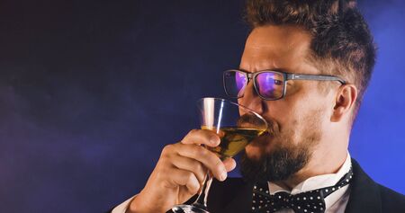 Handsome man in suit drinking champagne on black background. Portrait of elegance gentleman with glasses. Confident adult man in suit holding glass of champagne in studio. Luxury party.の写真素材
