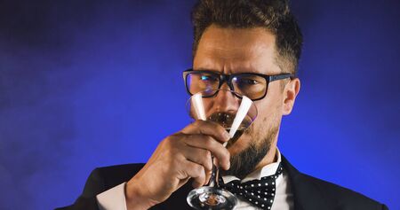 Handsome man in suit drinking champagne on black background. Portrait of elegance gentleman with glasses. Confident adult man in suit holding glass of champagne in studio. Luxury party.の写真素材