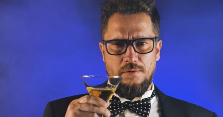 Handsome man in suit drinking champagne on black background. Portrait of elegance gentleman with glasses. Confident adult man in suit holding glass of champagne in studio. Luxury party.の写真素材