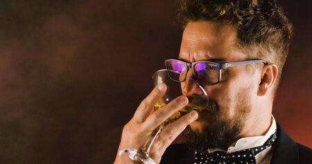 Handsome man in suit drinking champagne on black background. Portrait of elegance gentleman with glasses. Confident adult man in suit holding glass of champagne in studio. Luxury party.の写真素材