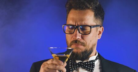 Handsome man in suit drinking champagne on black background. Portrait of elegance gentleman with glasses. Confident adult man in suit holding glass of champagne in studio. Luxury party.の写真素材