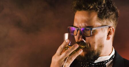 Handsome man in suit drinking champagne on black background. Portrait of elegance gentleman with glasses. Confident adult man in suit holding glass of champagne in studio. Luxury party.の写真素材