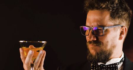 Handsome man in suit drinking champagne on black background. Portrait of elegance gentleman with glasses. Confident adult man in suit holding glass of champagne in studio. Luxury party.の写真素材