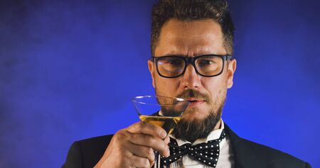 Handsome man in suit drinking champagne on black background. Portrait of elegance gentleman with glasses. Confident adult man in suit holding glass of champagne in studio. Luxury party.の写真素材