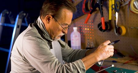 Senior craftsman working in his workshop. Portrait of pleasing old man working in modern industrial workshop. Close up shot of old mechanic master working in his workshop. Small business.の写真素材