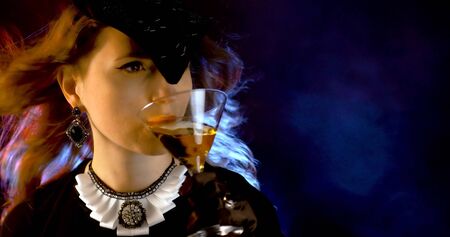 Portrait of vintage woman in classic hat drinking champagne on black background. Retro styling girl holding glass of champagne in studio. Retro portrait of a fashion elegance model. Luxury party.の写真素材