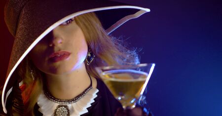 Portrait of vintage woman in classic hat drinking champagne on black background. Retro styling girl holding glass of champagne in studio. Retro portrait of a fashion elegance model. Luxury party.の写真素材