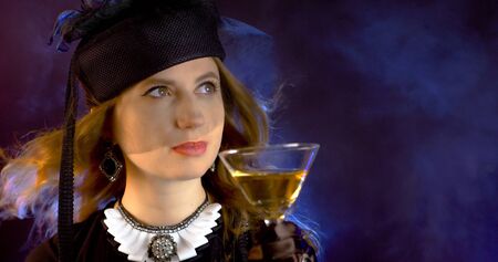 Portrait of vintage woman in classic hat drinking champagne on black background. Retro styling girl...