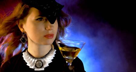 Portrait of vintage woman in classic hat drinking champagne on black background. Retro styling girl holding glass of champagne in studio. Retro portrait of a fashion elegance model. Luxury party.の写真素材