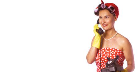 Cheerful housewife in pin up style speaks on the phone. Expressive lady in a red dress and a yellow household gloves. Housework or cleaning conceptの写真素材