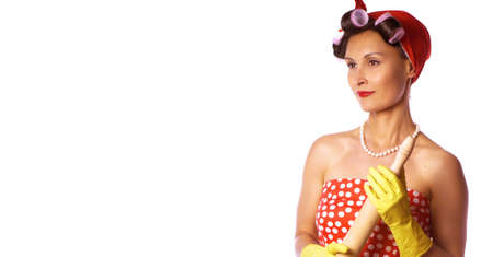 Cheerful housewife in pin up style with perfect hair and make up. Retro lady in a red dress and a yellow household gloves with a rolling pin. Housework, cleaning, cooking concept.の写真素材