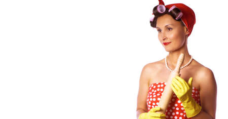 Cheerful housewife in pin up style with perfect hair and make up. Retro lady in a red dress and a yellow household gloves with a rolling pin. Housework, cleaning, cooking concept.の写真素材