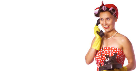 Cheerful housewife in pin up style speaks on the phone. Expressive lady in a red dress and a yellow household gloves. Housework or cleaning conceptの写真素材